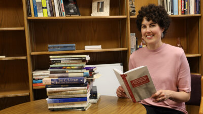 Woman reading book next to stack of other books