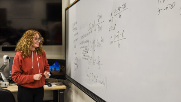 A student finishes writing a math formula on the whiteboard.