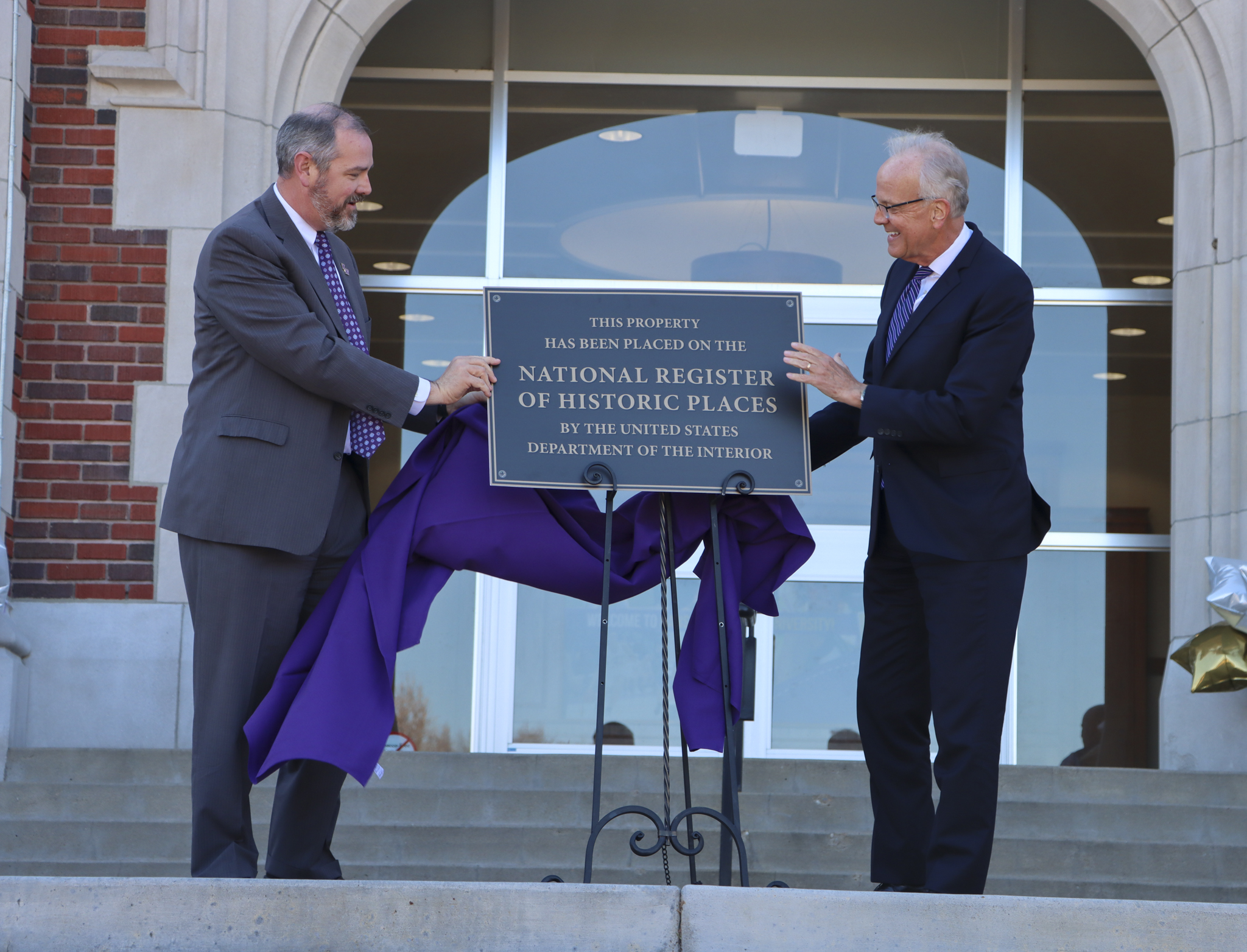 Two men in suits unveiling sign